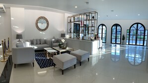 A modern living room with a sofa, coffee table, and ottomans, a round mirror, and a glass partition with decorative items. - The Seens Hotel (Krabi)