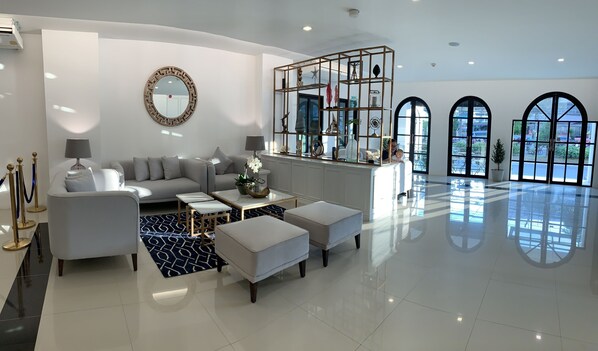 A modern living room with a sofa, coffee table, and ottomans, a round mirror, and a glass partition with decorative items.