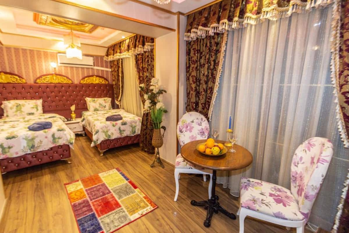 Habitación de hotel con dos camas, una mesa redonda con fruta, una silla y un tapete decorativo.