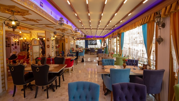 A restaurant with a classic interior, featuring marble floors, ornate ceiling details, and a variety of seating arrangements including round tables and upholstered chairs.