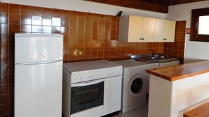 A compact kitchen with a refrigerator, oven, washing machine, and wooden cabinets. - AffittaSardegna - Trilo Bellavista 1 (Olbia)