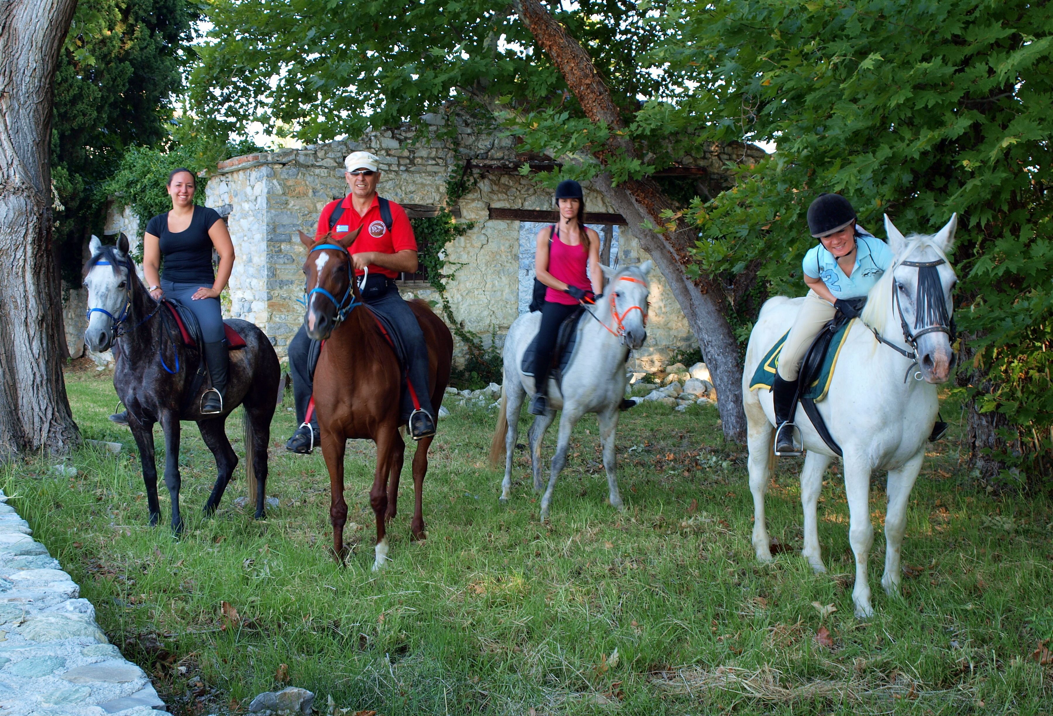 Quatre personnes à cheval, sur un sentier herbeux bordé de murs de pierre et avec des arbres en arrière-plan.