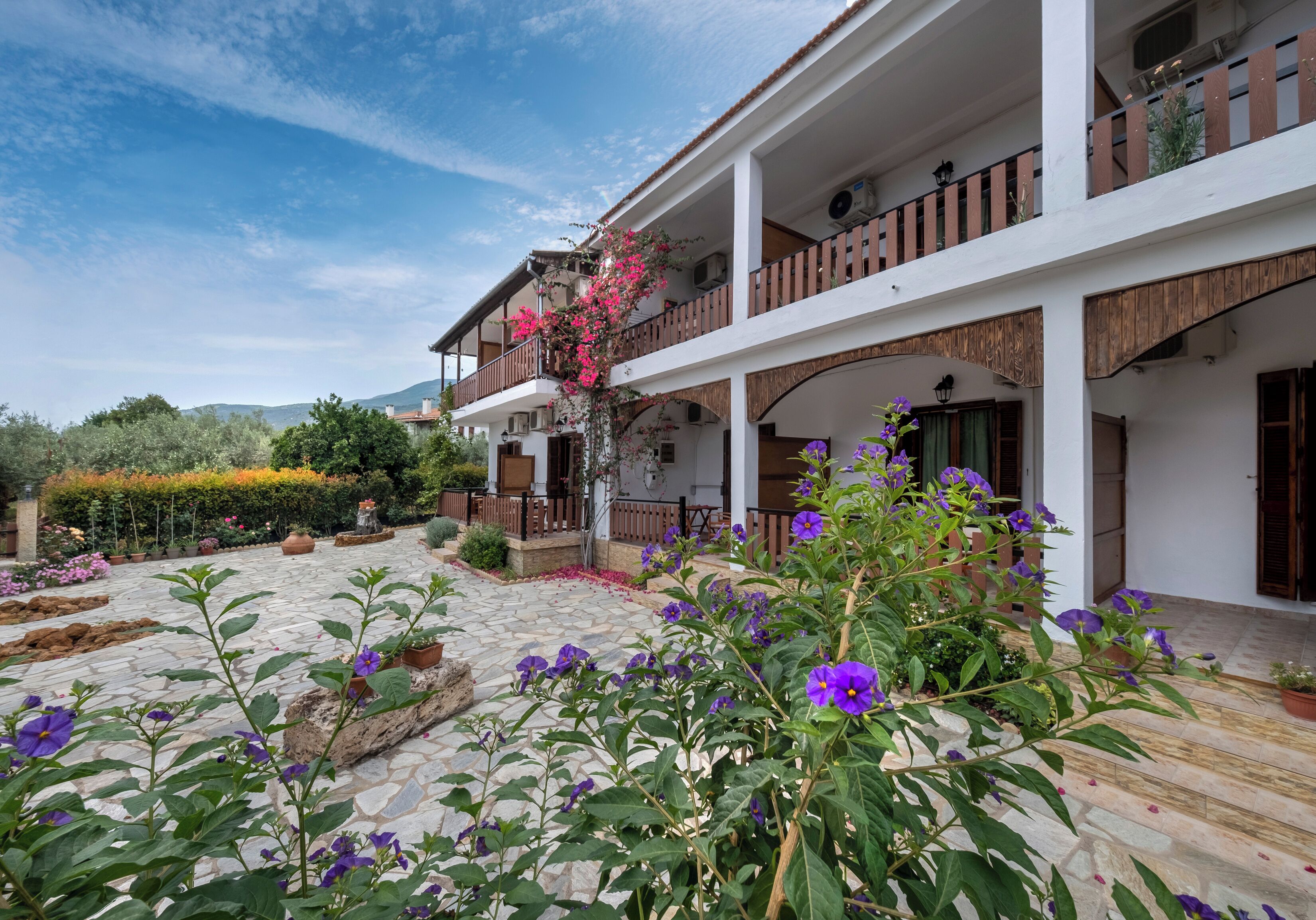 A two-story building with a stone courtyard, balconies with wooden railings, and potted plants.
