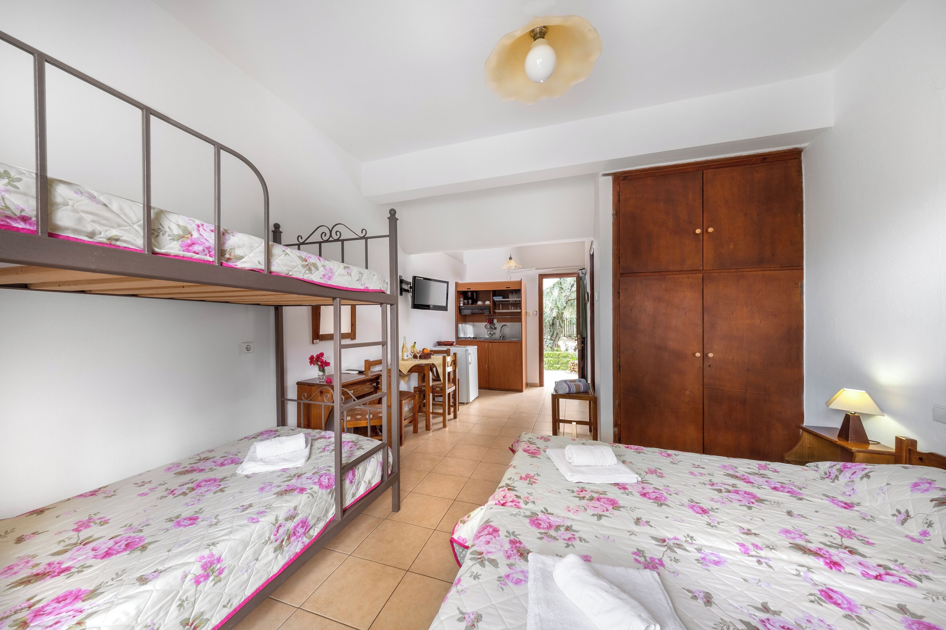 A room with bunk beds, a desk, a chair, a television, a wardrobe, and a lamp.
