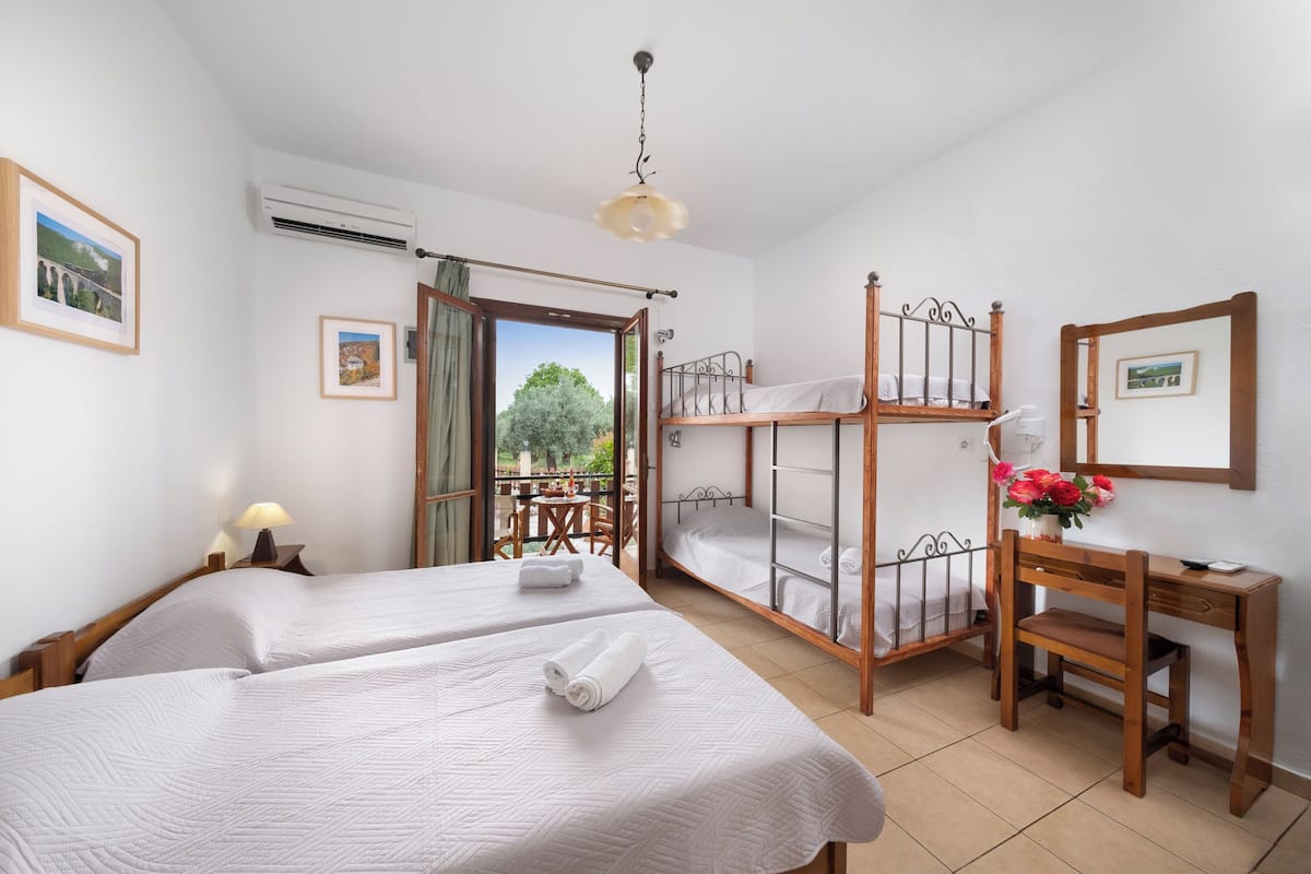 A bedroom with two beds, a desk, and a balcony.