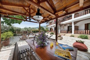 A wooden pergola with a hanging light fixture, a table with a vase of flowers, and a view of a white building with balconies. - Vergonis Studios (South Pelion)