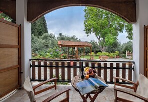 A wooden deck with a table set for two, overlooking a garden with a gazebo and potted plants. - Vergonis Studios (South Pelion)