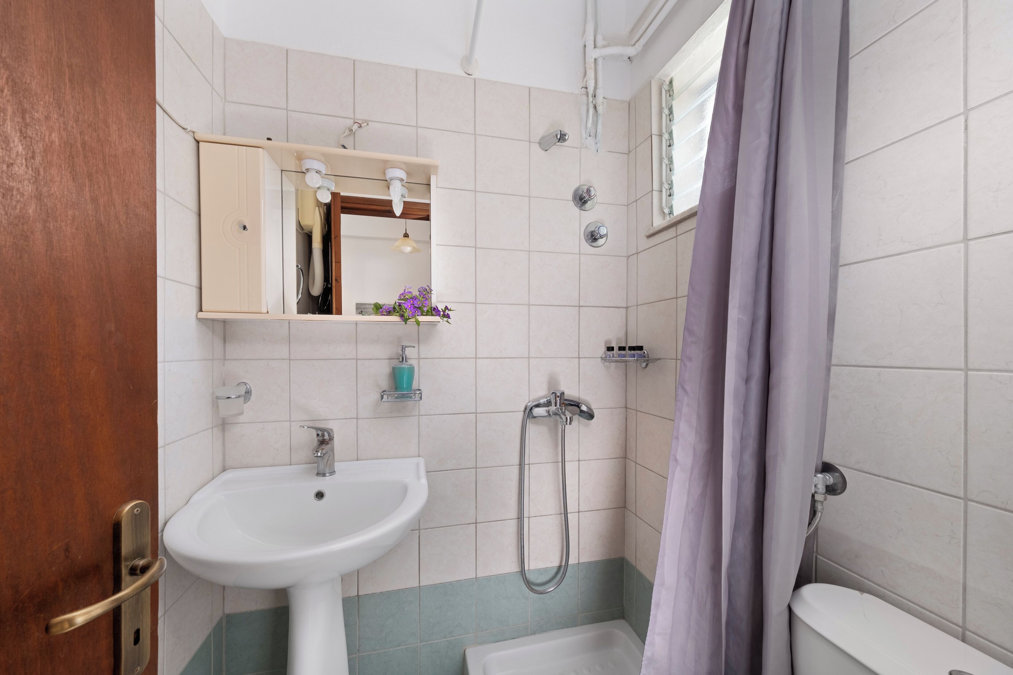 Un baño con lavamanos blanco, espejo, ducha e inodoro.