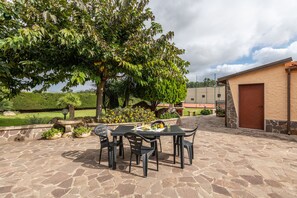 An outdoor patio with stone flooring, a table with chairs, and a building with a brown door.