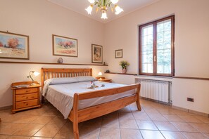 A bedroom with a wooden bed, bedside tables, a radiator, and a window with a view.