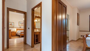 A hotel room with a wooden door, a bathroom with a mirror and sink, and a bed with a wooden headboard. - AffittaSardegna - Villetta Tennis 1 (Alghero)