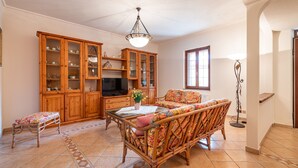 A living room with a wooden cabinet, a television, a sofa, and a patterned bench. - AffittaSardegna - Villetta Tennis 1 (Alghero)