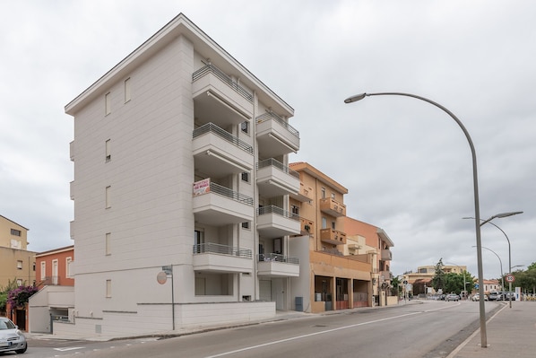 Un edificio de varios pisos con balcones, una calle en su parte delantera y una señal de límite de velocidad.