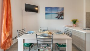 Ein Essbereich mit einem für vier Personen gedeckten Tisch, einem an der Wand montierten Fernseher und einem Gemälde mit einer Strandansicht darüber.