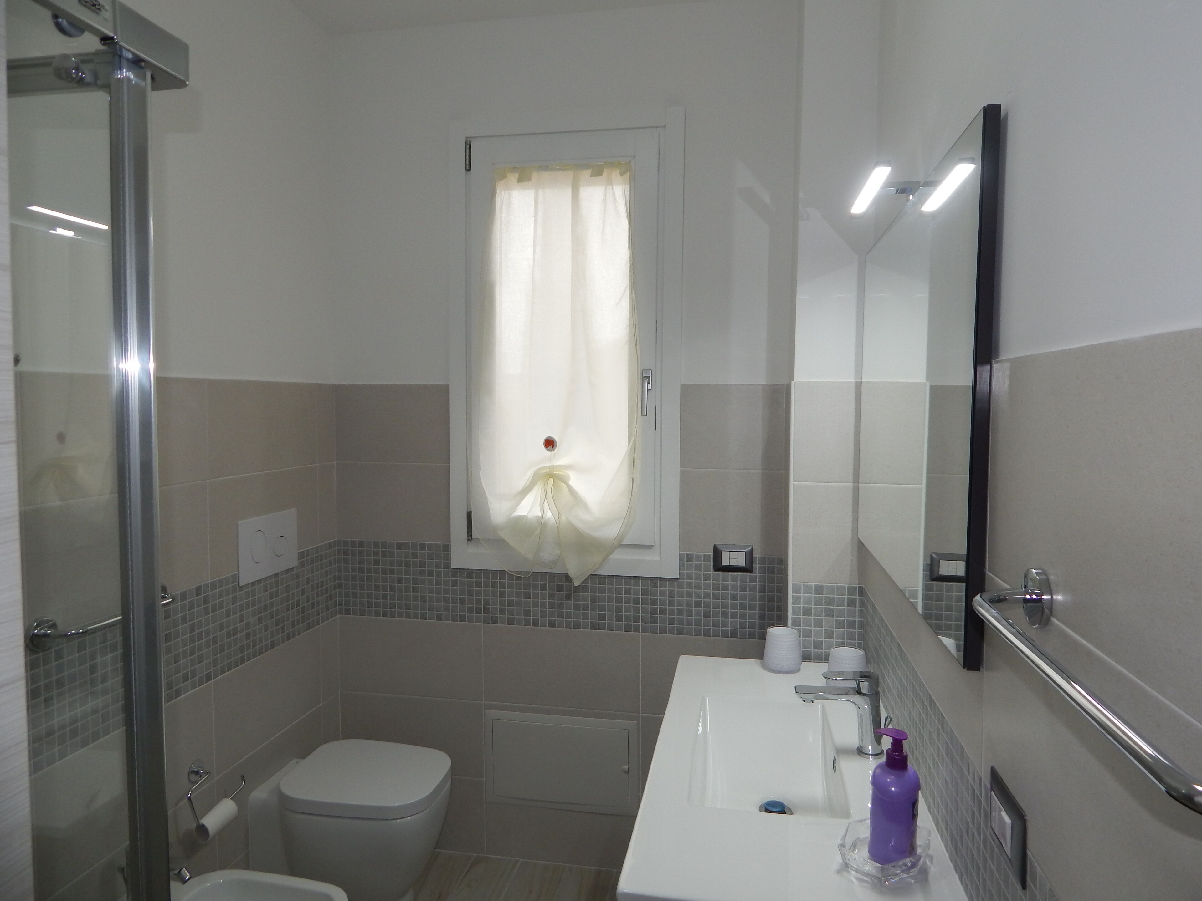 A bathroom with a shower, toilet, sink, and a window with a curtain.