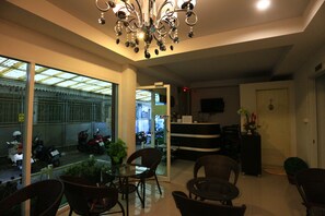 A hotel lobby with wicker furniture, a reception desk, a TV, and a view of the street through glass doors. - Bann Bunga (Bangkok)