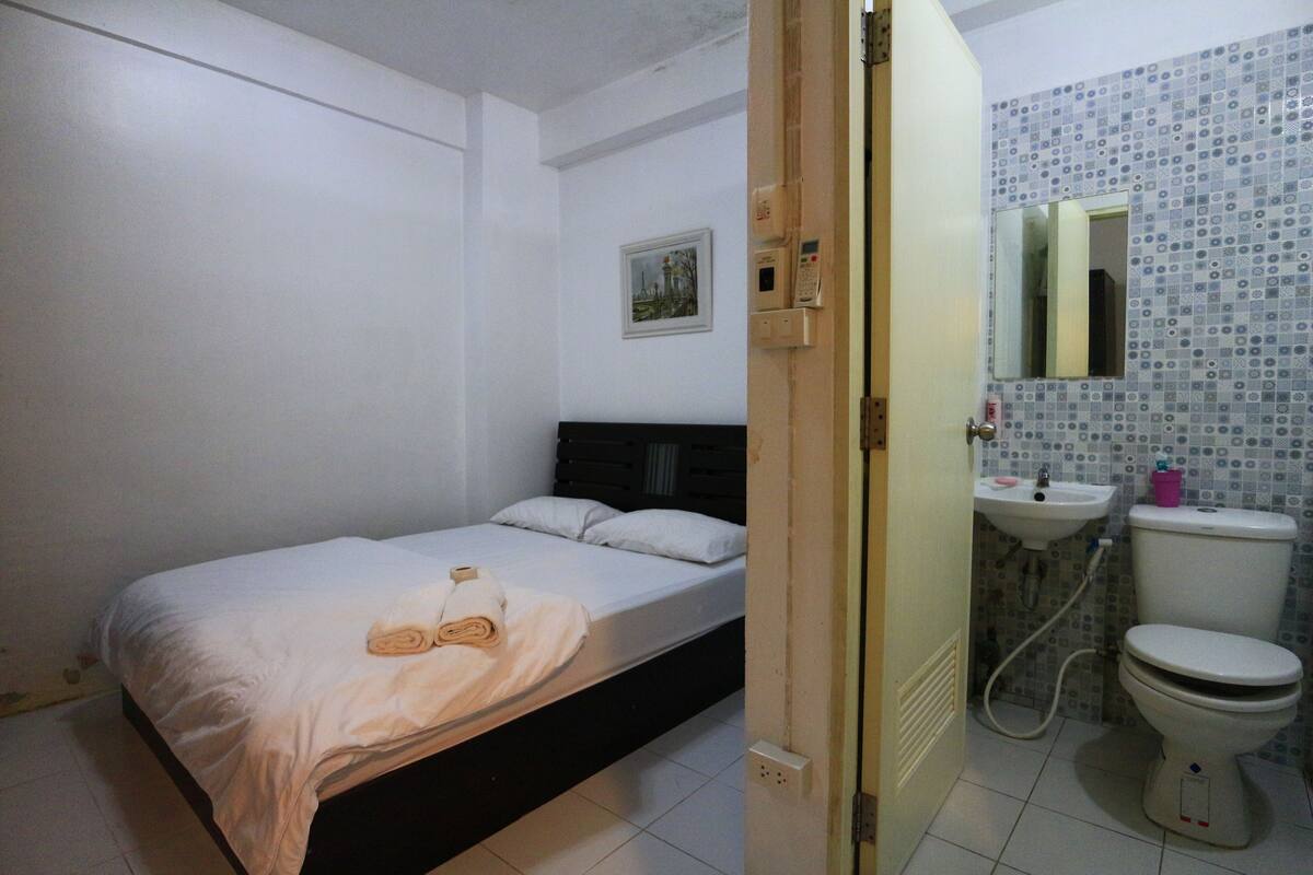 A bedroom with a bed, a bedside table, and a bathroom with a toilet and sink.