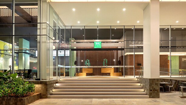 Een moderne hotel lobby met een glazen gevel, een receptiebalie en een trap naar de bovenverdieping.
