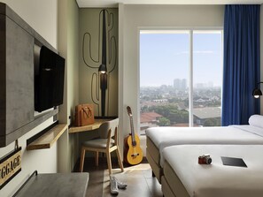 A hotel room with a bed, a desk with a chair, a guitar, a television, and a view of the city. - ibis Styles Jakarta Simatupang (Jakarta)