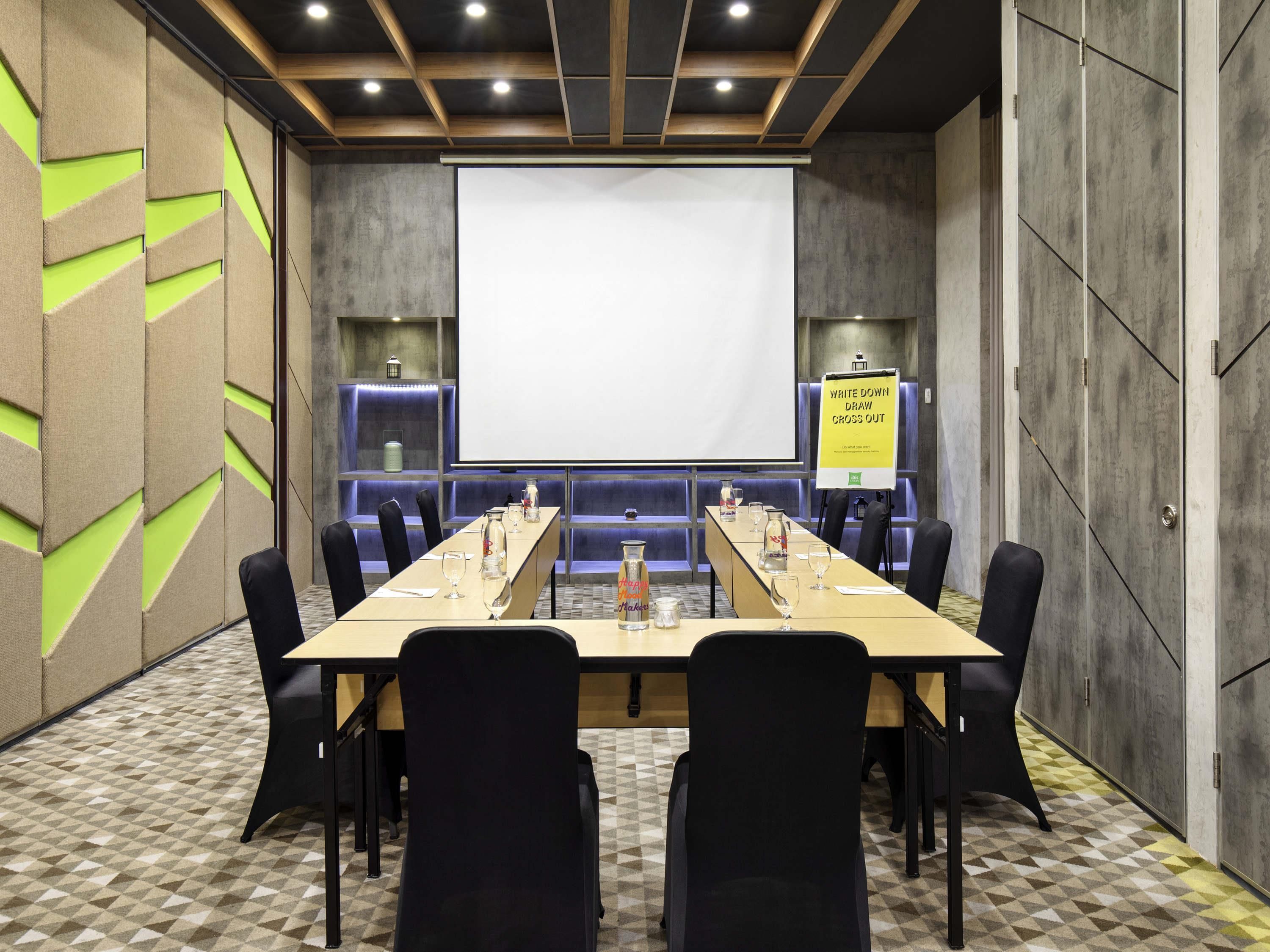 A conference room with a long table, black chairs, a projector screen, and a whiteboard.