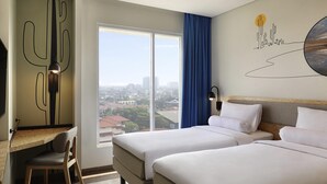 Habitación de hotel con dos camas, un escritorio, una silla y un amplio ventanal con vistas a la ciudad.