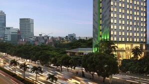 A high-rise hotel with a prominent green logo, surrounded by a busy urban street and other buildings. - ibis Styles Jakarta Simatupang (Jakarta)