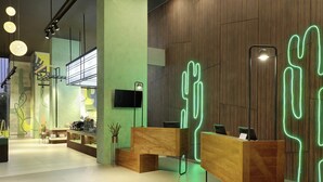 A modern reception area with wooden reception desks, a flat-screen TV, and a cactus-shaped neon light. - ibis Styles Jakarta Simatupang (Jakarta)