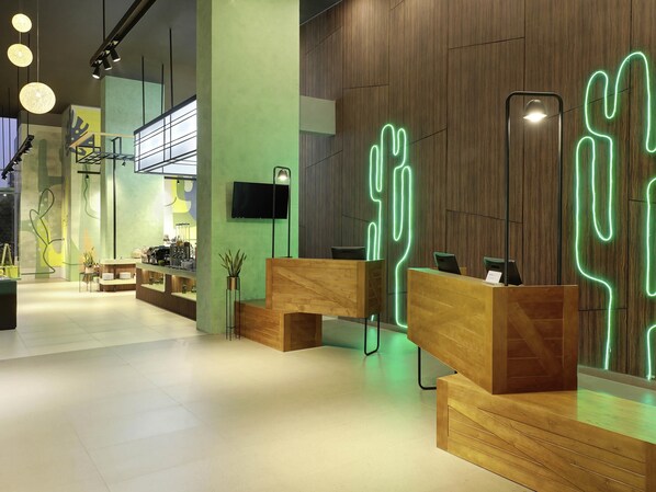 A modern reception area with wooden reception desks, a flat-screen TV, and a cactus-shaped neon light. - ibis Styles Jakarta Simatupang (Jakarta)