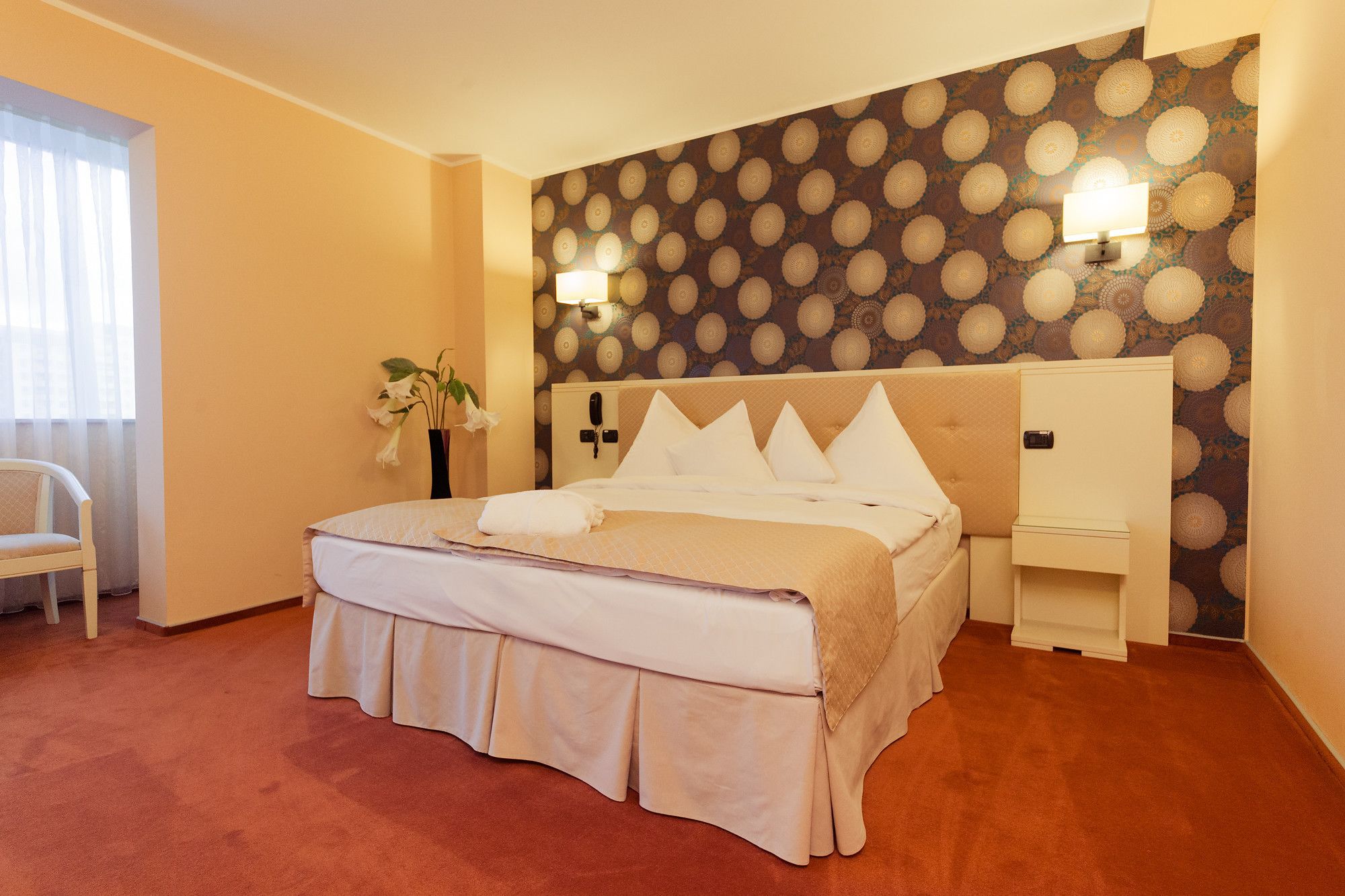 Una habitación de hotel con cama, mesita de noche y una pared con un diseño circular.