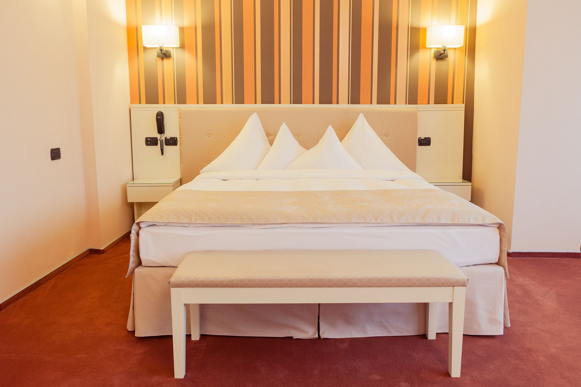 A hotel room with a bed, bedside tables, a bench, and wall-mounted lamps.