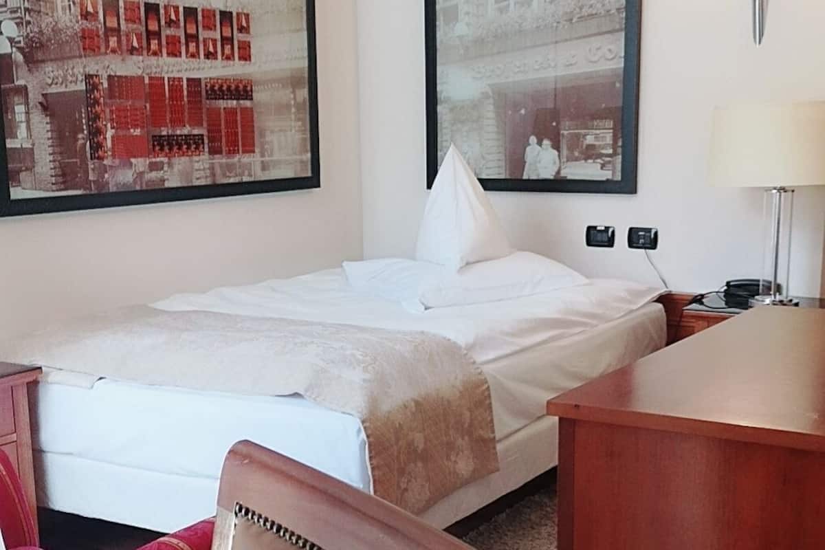 Une chambre d’hôtel avec un lit, un bureau, une chaise et deux tableaux encadrés au mur.