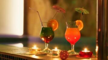 Zwei Cocktails mit Trinkhalmen und Garnituren auf einer Bar, umgeben von Kerzen.