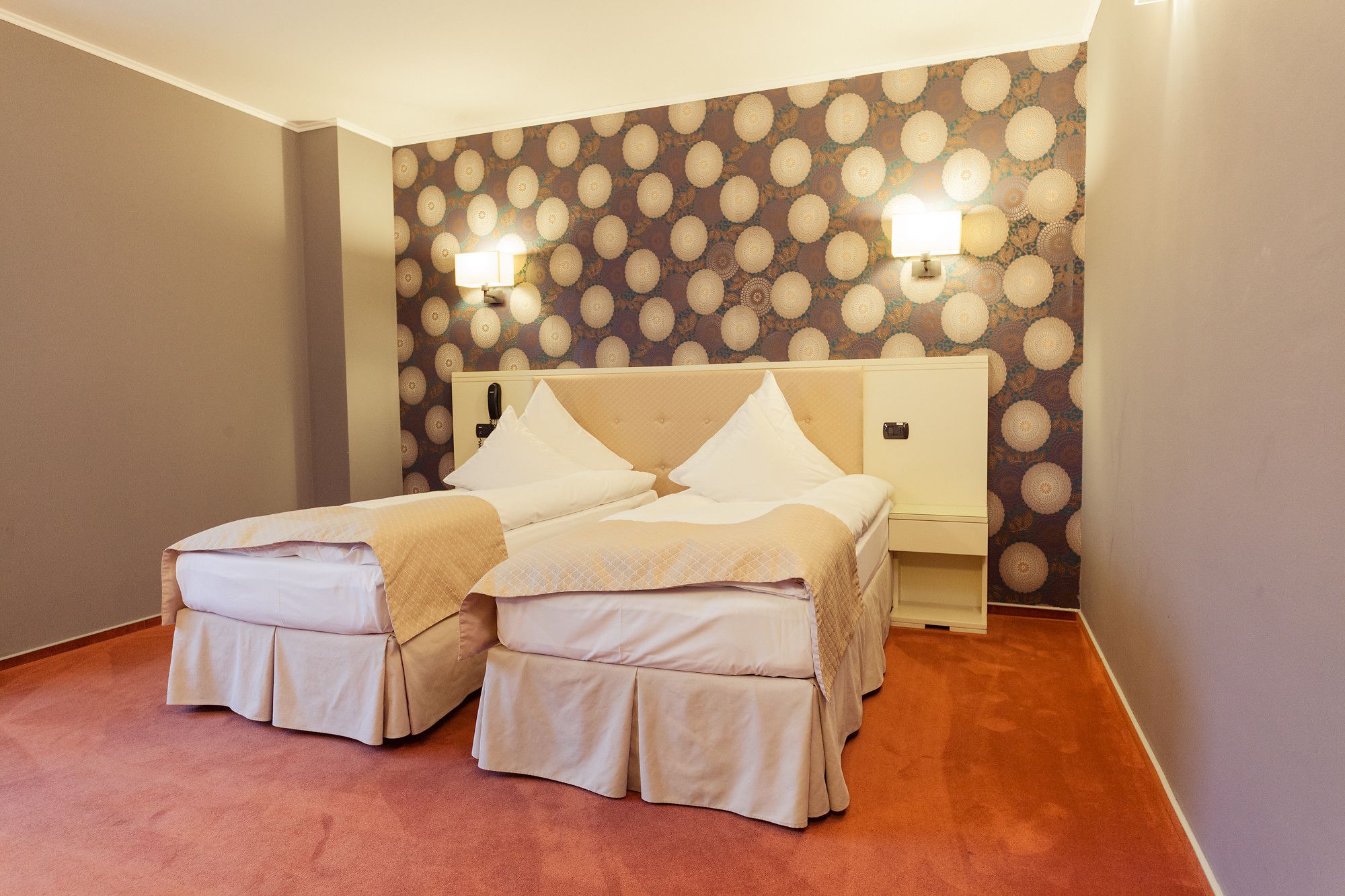 Habitaci ón doble con dos camas, un papel tapiz estampado y dos lámparas fijadas a la pared.