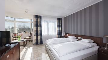 Ein Hotelzimmer mit einem großen Bett, einem Fernseher, einem Schreibtisch mit Stuhl und einem Fenster mit Vorhängen.