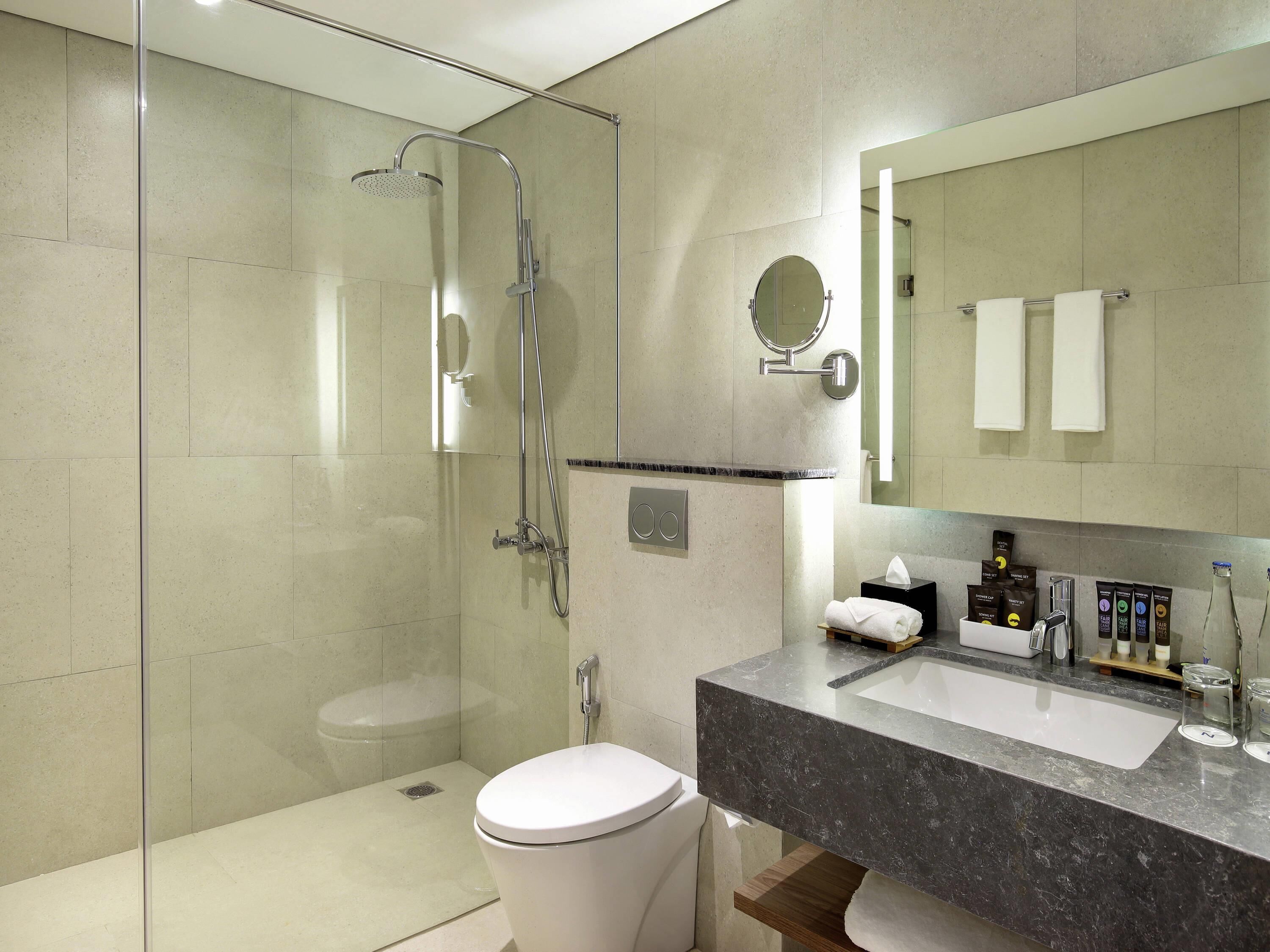 A modern bathroom with a glass-enclosed shower, a toilet, a sink with toiletries, and a mirror.