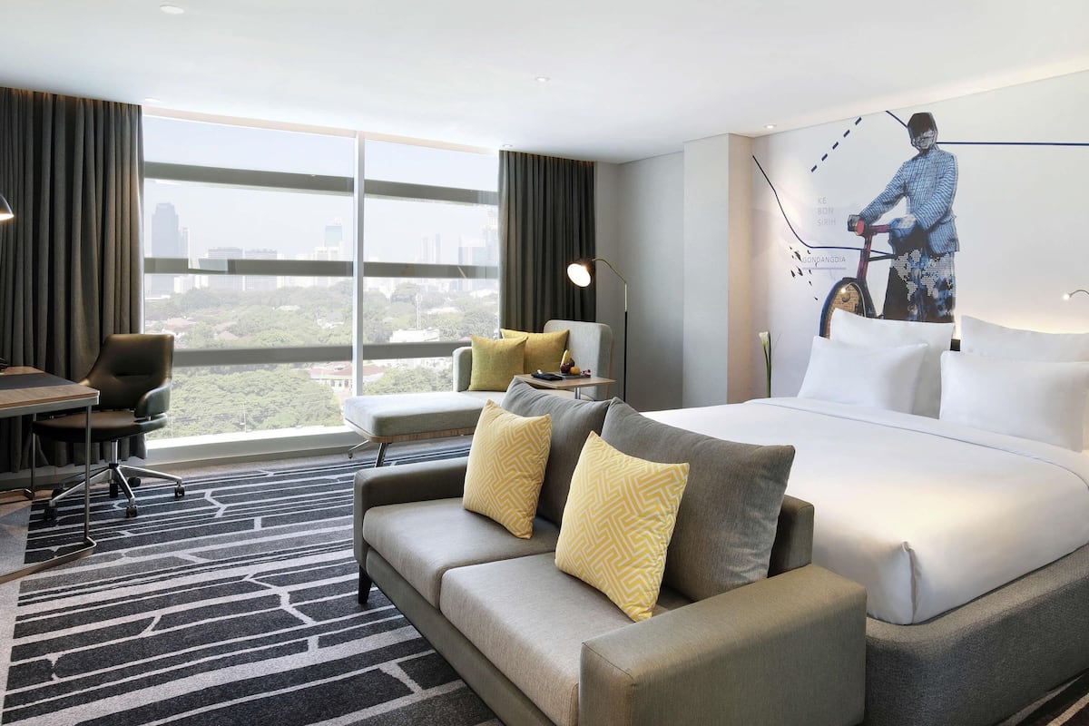 Ein Hotelzimmer mit großem Fenster, einer Couch, einem Bett, einem Schreibtisch und einem Sessel.