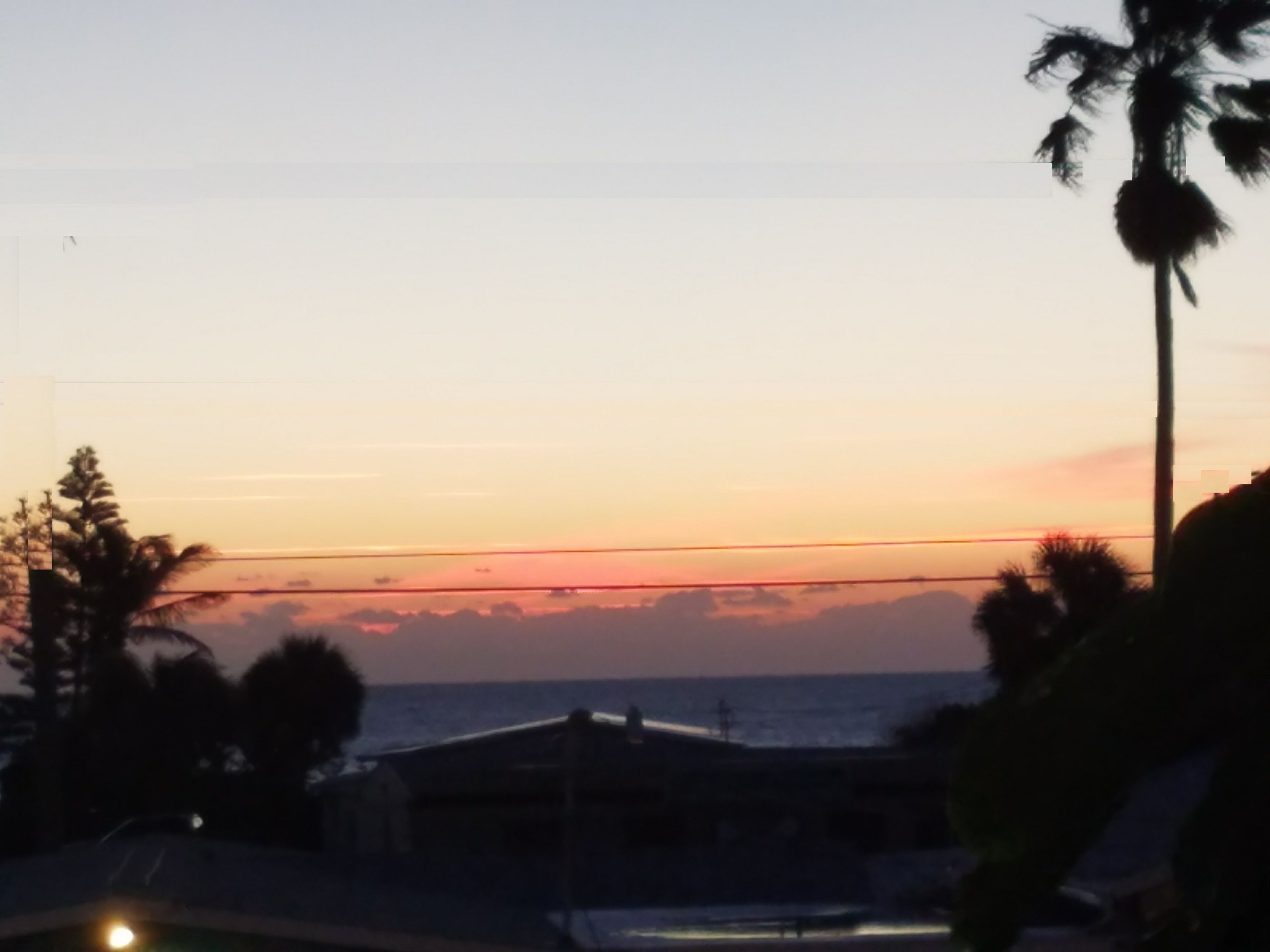 Une vue sur le coucher de soleil en bord de mer, avec une maison et des palmiers.