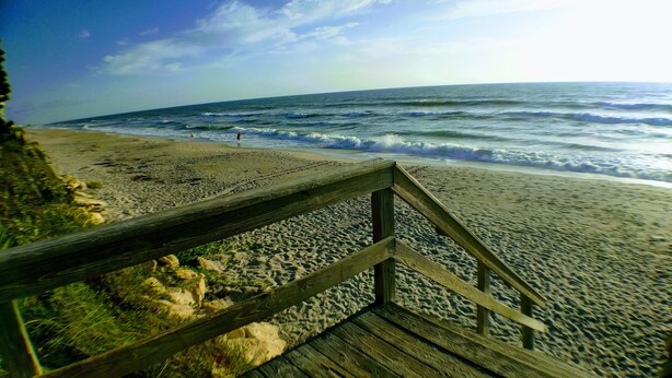 A wooden boardwalk leading to a sandy beach with waves. - The Sand Castle (Satellite Beach)