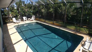 An indoor swimming pool with clear water, surrounded by a covered area with chairs and a view of the outdoors. - The Sand Castle (Satellite Beach)