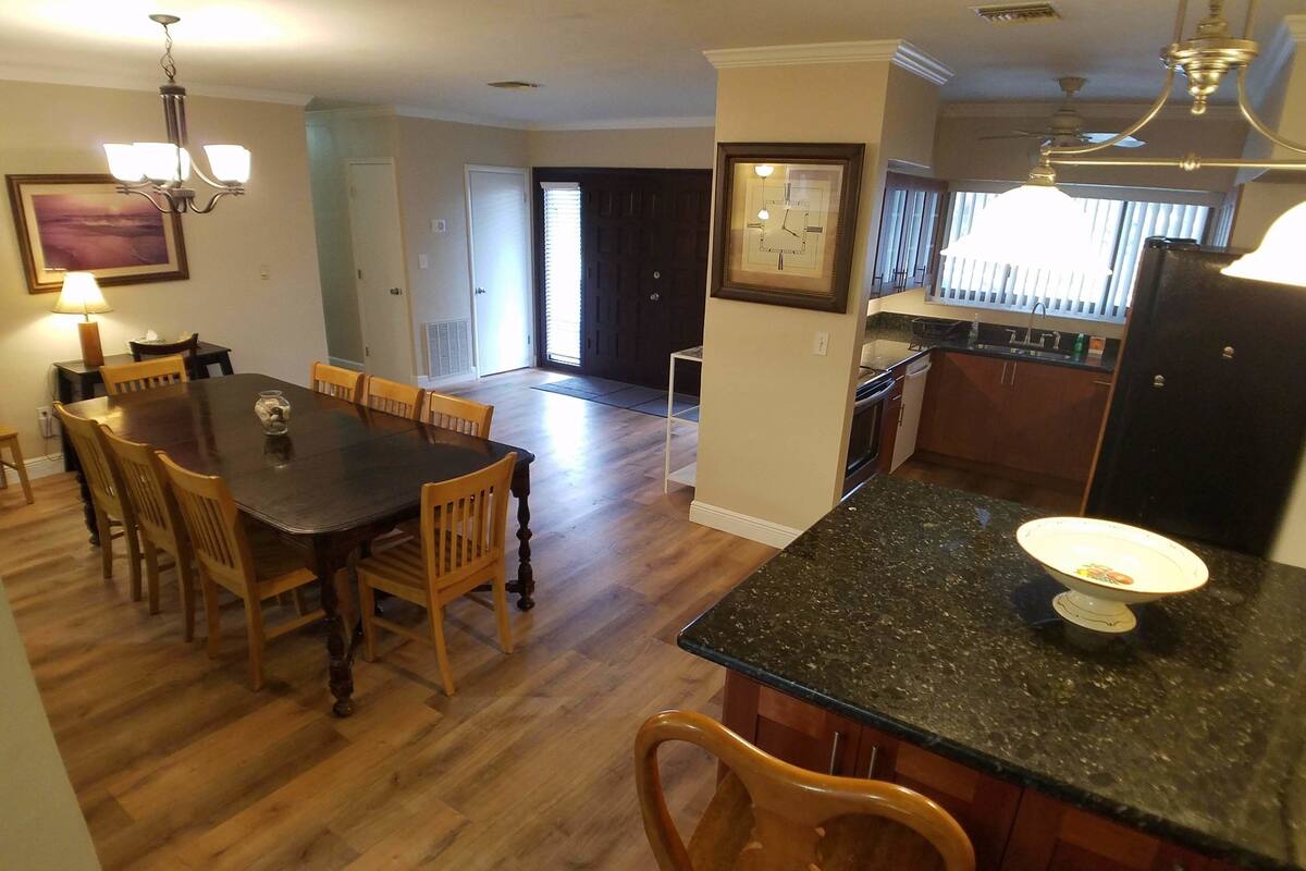 A spacious kitchen with a granite countertop, wooden dining table, and chairs.