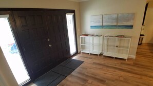 A hallway with a dark wooden door, a doormat, and white shelving units against the wall. - The Sand Castle (Satellite Beach)