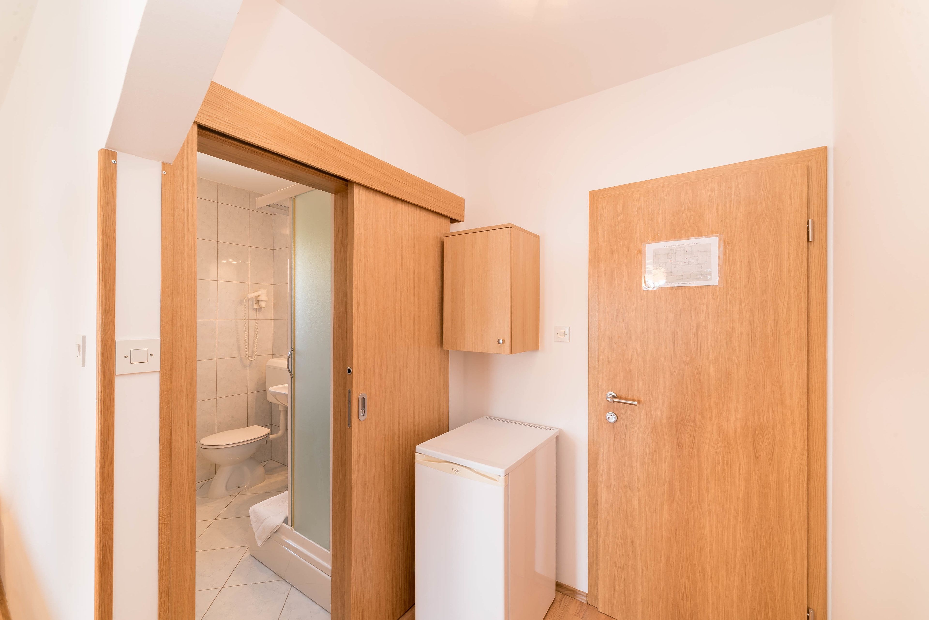 A compact bathroom with a toilet, shower, and a small white refrigerator.
