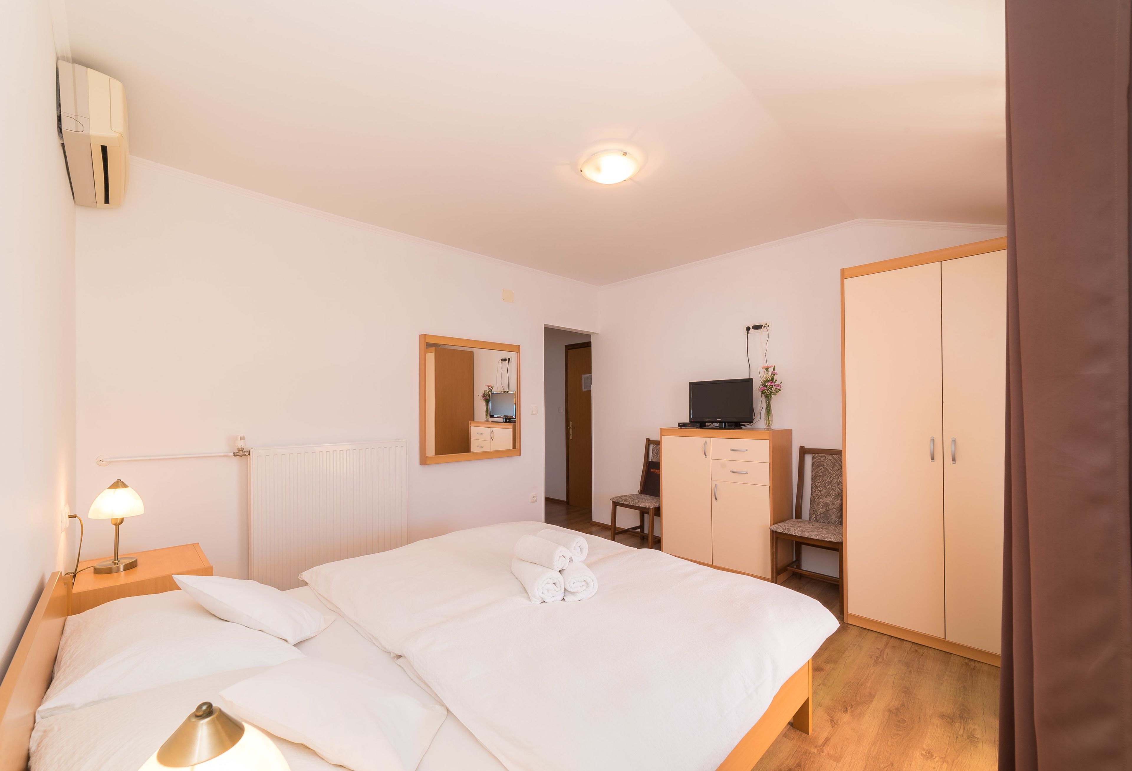 A hotel room with a bed, bedside lamps, a mirror, a wardrobe, and a television.