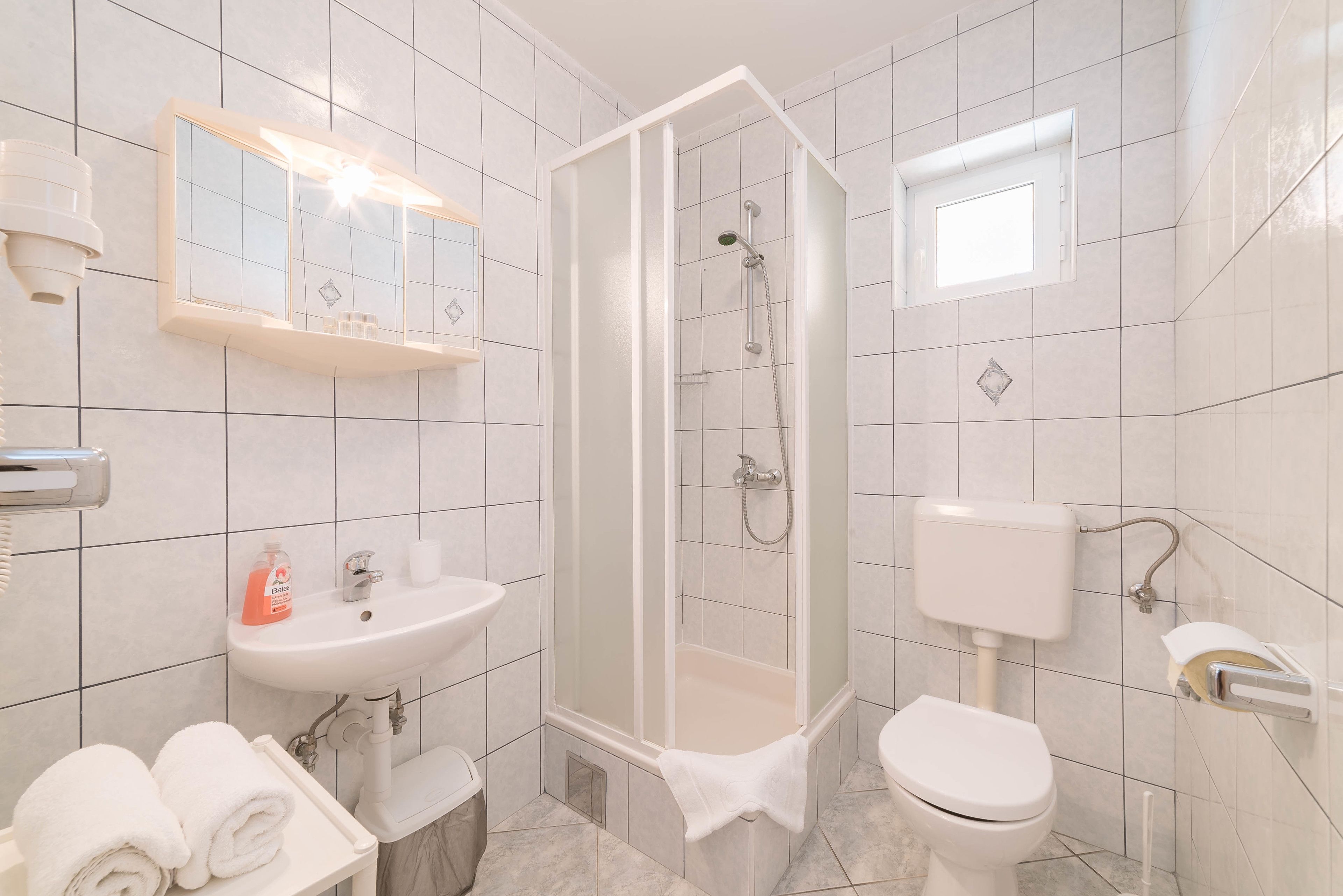 A bathroom with a shower, sink, toilet, and a mirror with lights.