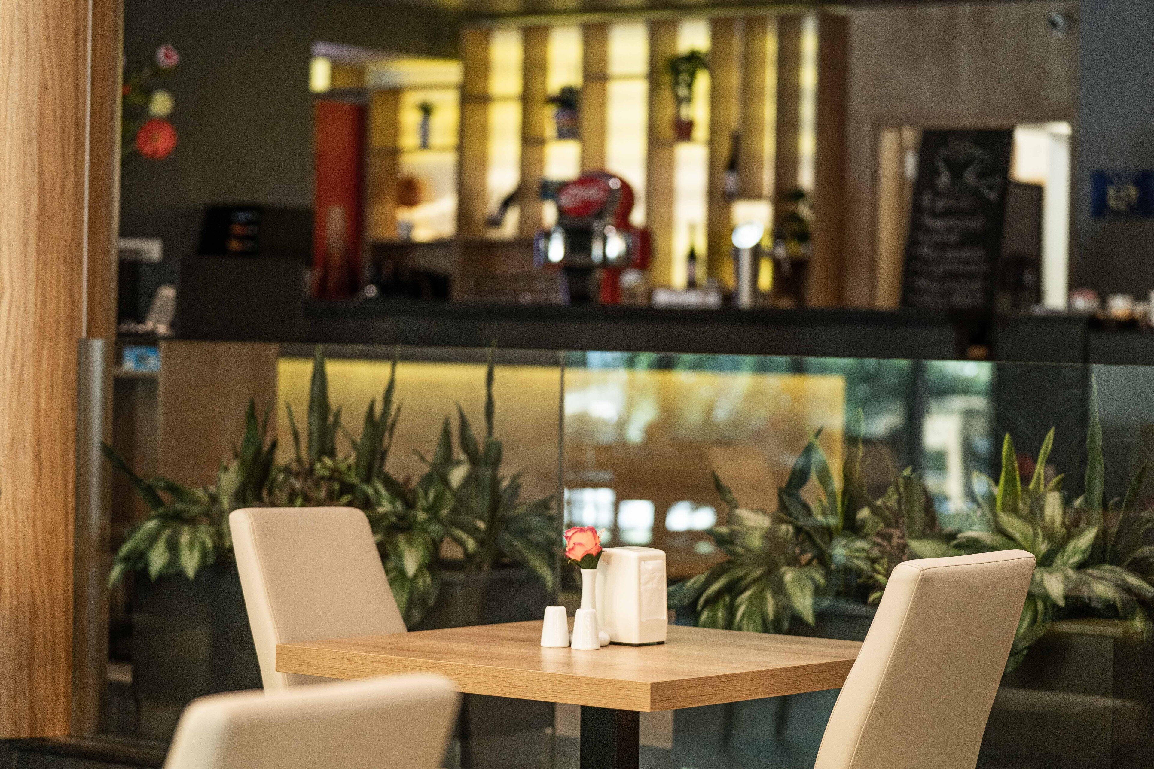 A restaurant with a bar area in the background, featuring a modern design with plants and a wooden table with chairs.
