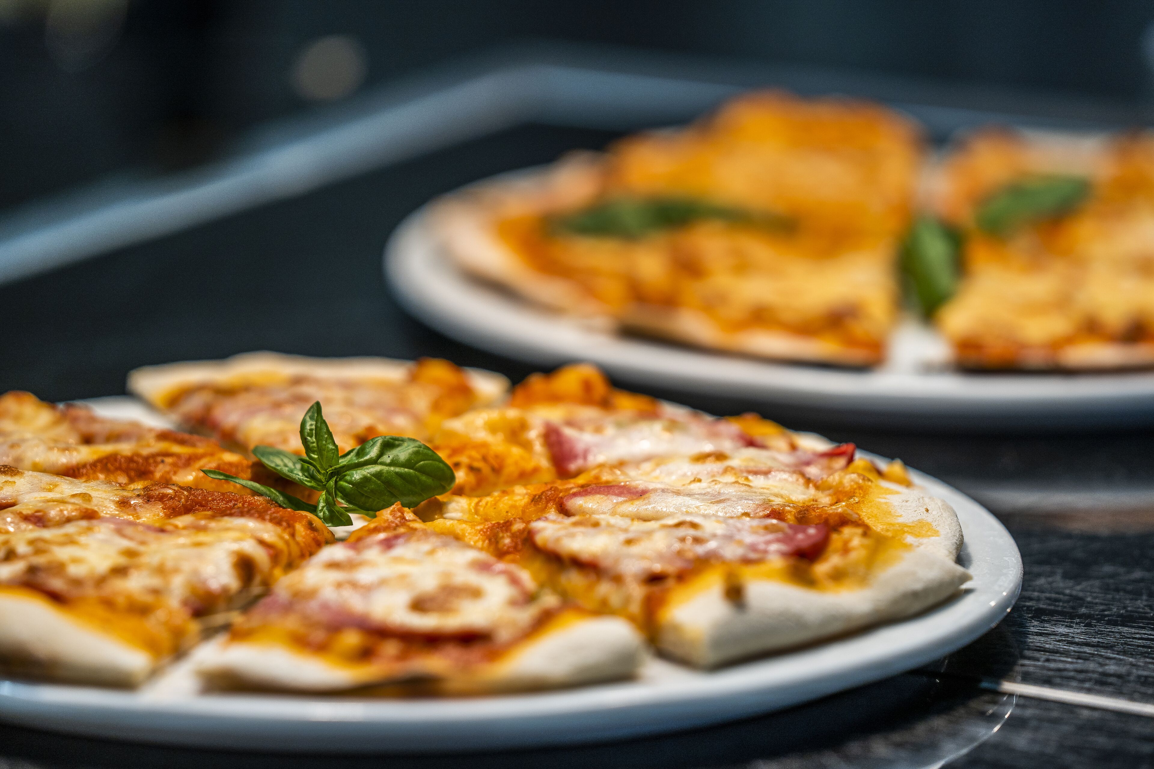 A plate of pizza with cheese and ham, garnished with basil leaves.