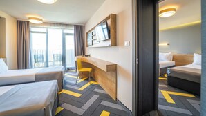 Habitación de hotel con dos camas, un escritorio, una silla, un televisor y un balcón con cortinas.