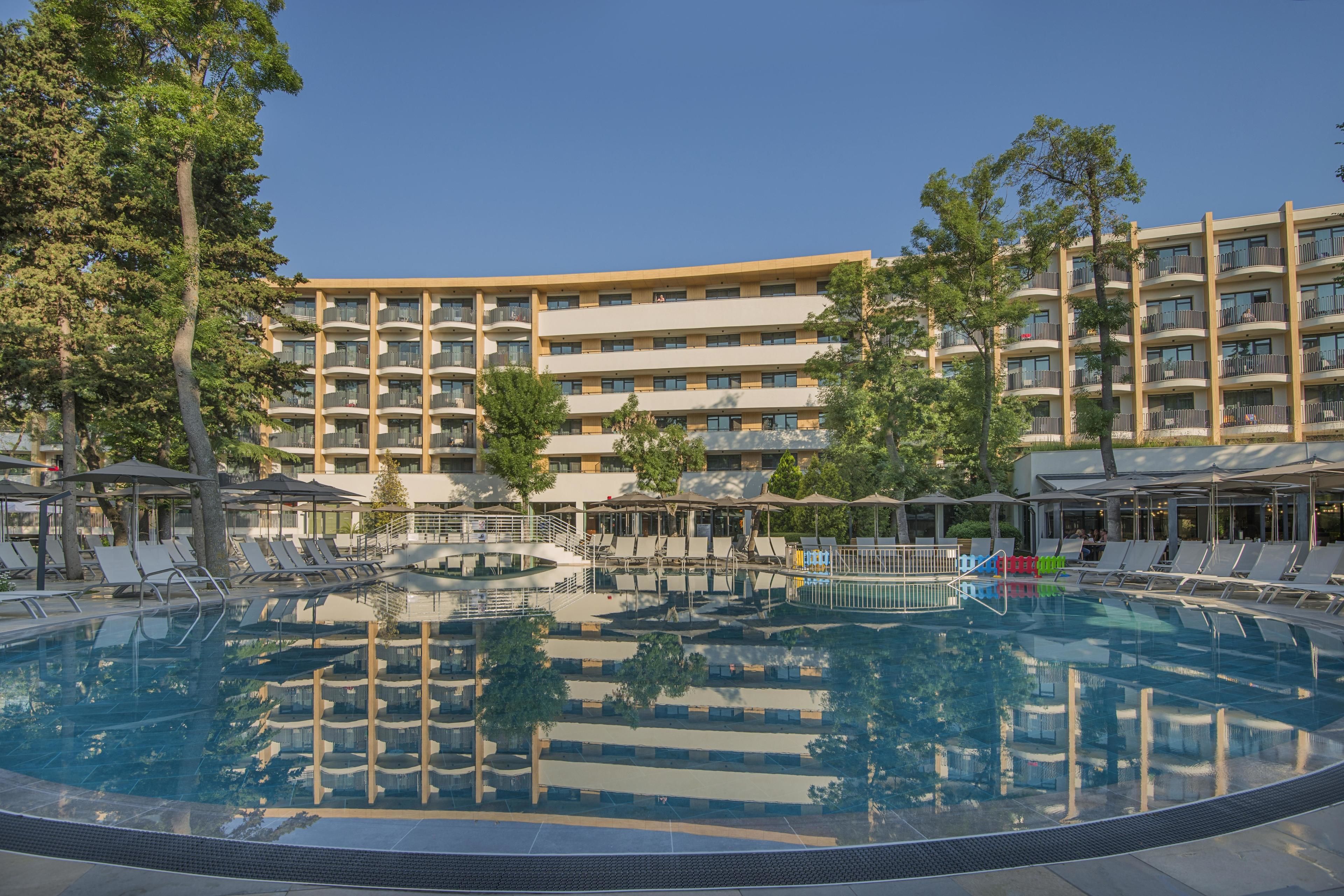 A hotel with a large pool, multiple balconies, and outdoor seating areas.
