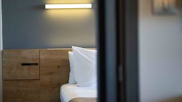 A hotel room with a wooden headboard, a bed with white bedding, and a wall-mounted light fixture.