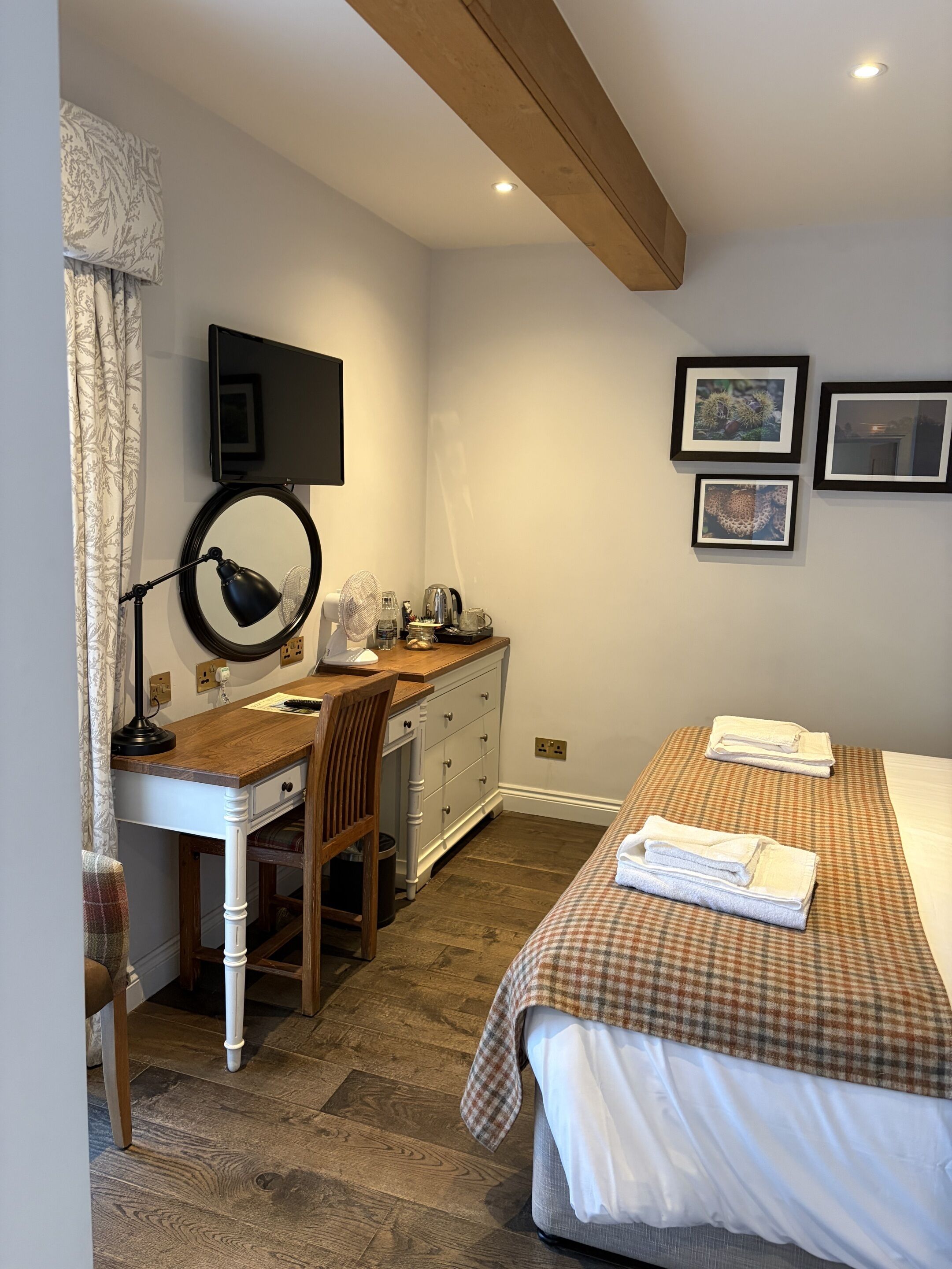 Une chambre à coucher comprenant un lit, un bureau avec une chaise, un téléviseur fixé au mur et deux tableaux encadrés.